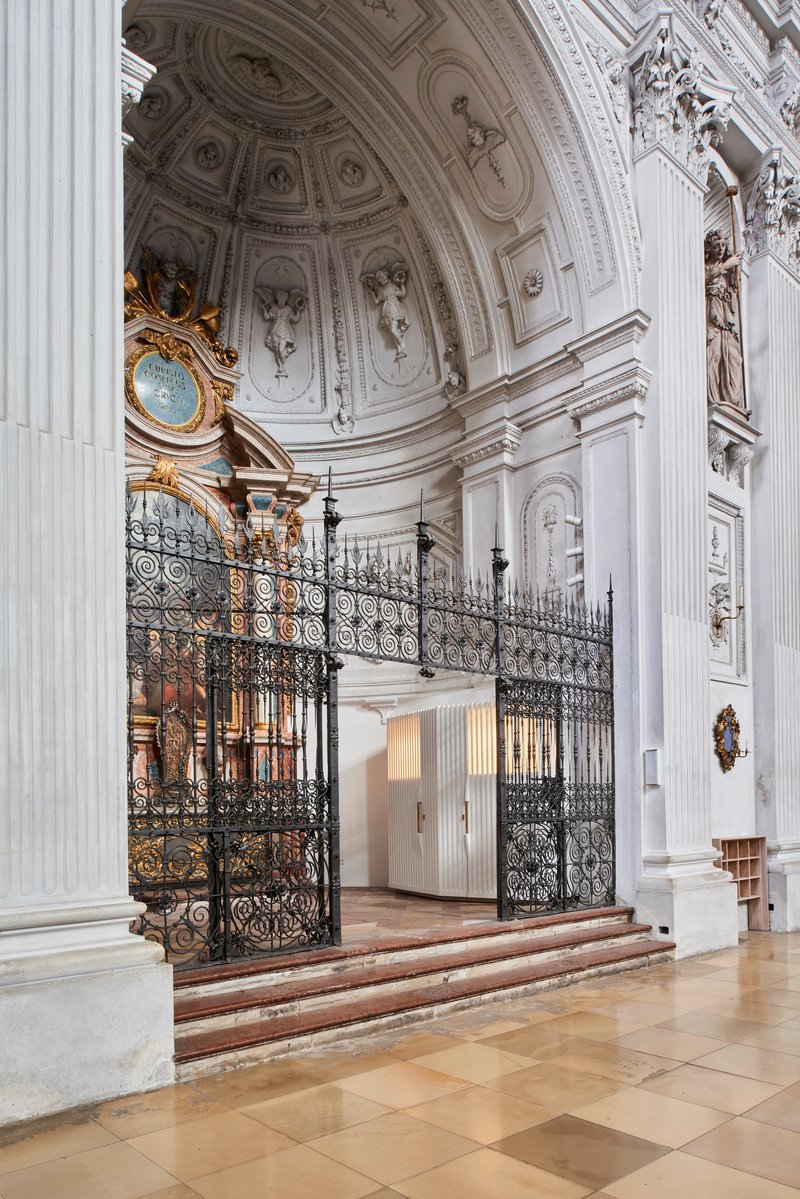 Curved white ribbed enclosure beneath a coffered dome with ornamental plasterwork and a gilded clock
