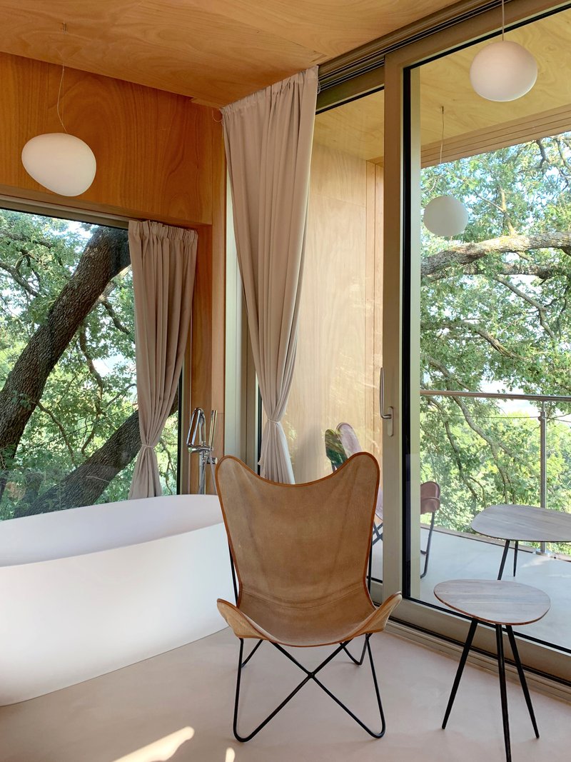 Corner room with floor-to-ceiling glazing opening to terrace among tree branches