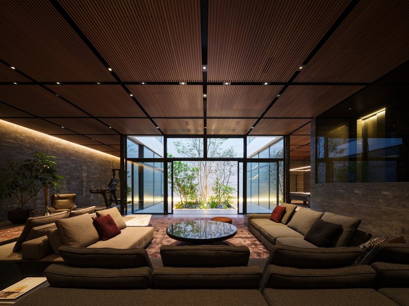 Seating area beneath gridded timber ceiling with full-height glazed walls framing courtyard garden at dusk
