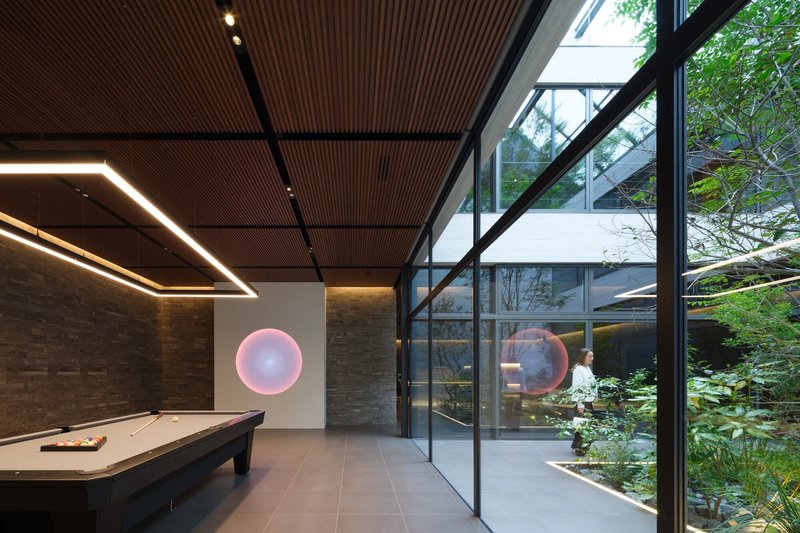 Pool table room with pink circular light installation and glazed walls revealing lush courtyard planting