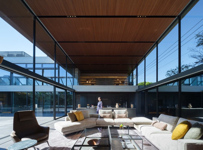 Interior courtyard with slatted timber ceiling, glass walls and sectional seating under afternoon sun