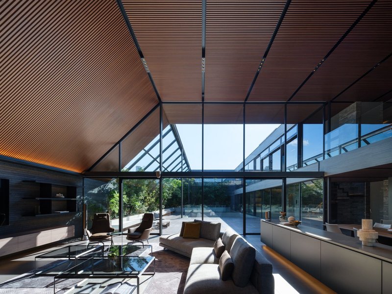 Living space with timber-slatted ceiling, full-height glazing and glimpse of central water feature
