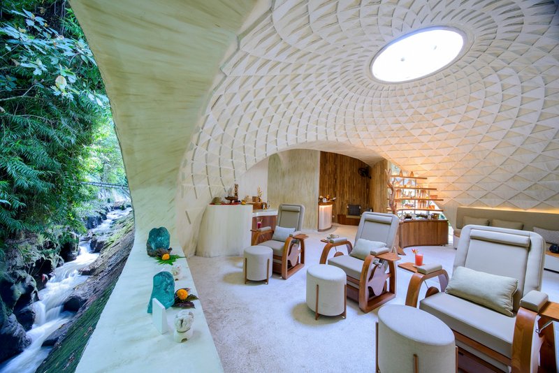 Vaulted interior with woven bamboo ceiling and central oculus opening to waterfall and jungle beyond