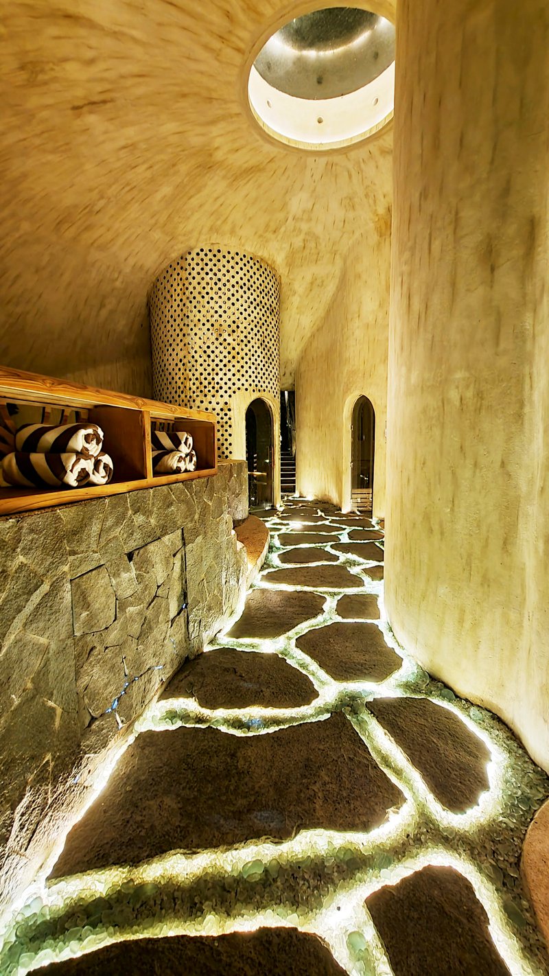 Corridor with irregular stone floor joints and perforated bamboo cylinder beneath a circular skylight