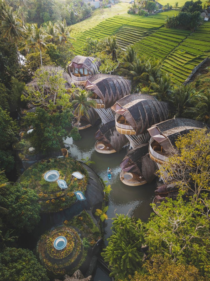 Aerial view of ribbed barrel-vault structures nestled among tropical gardens and terraced rice paddies