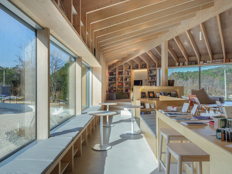 Reading area with floor-to-ceiling glazing overlooking bare winter trees and exposed timber ceiling beams