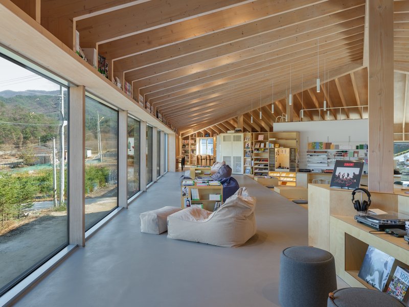 Long interior view showing exposed wood structure, glazed walls, and seating area with low tables
