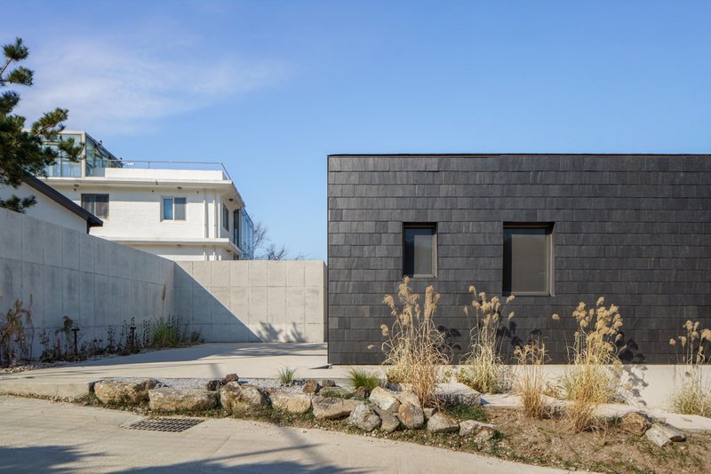 Courtyard view of dark stone tile volume with two small windows and winter grasses in foreground