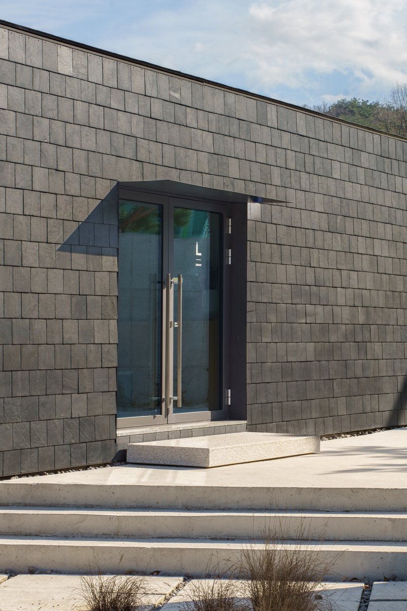 Recessed glass entrance with steel handles and canopy projecting from grey stone tile wall