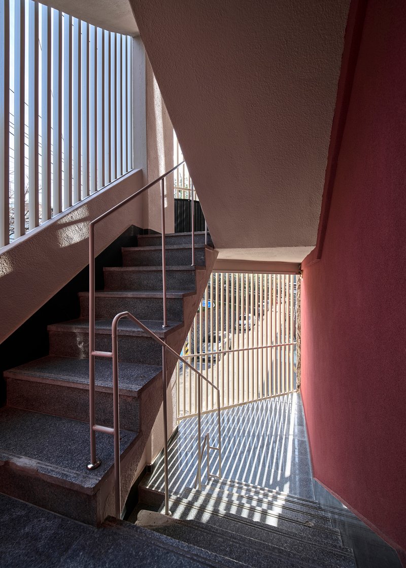 Stairwell with vertical slat screens casting striped shadows across terrazzo steps and maroon walls