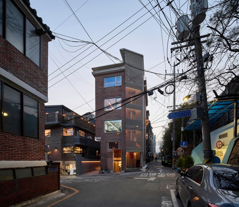 Narrow brick tower rising among low neighbors beneath a web of overhead utility wires at dusk