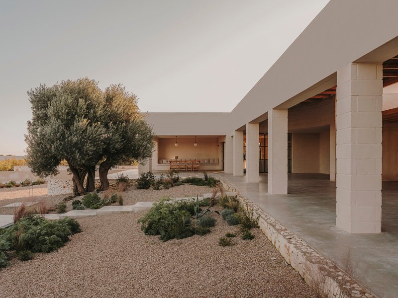 Courtyard with gravel and planted beds beside a covered colonnade at dusk
