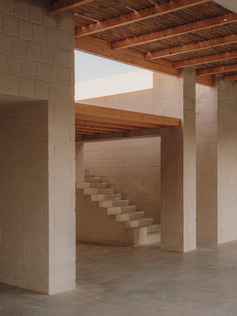 Interior view of cantilevered stone staircase through masonry columns under exposed timber joists