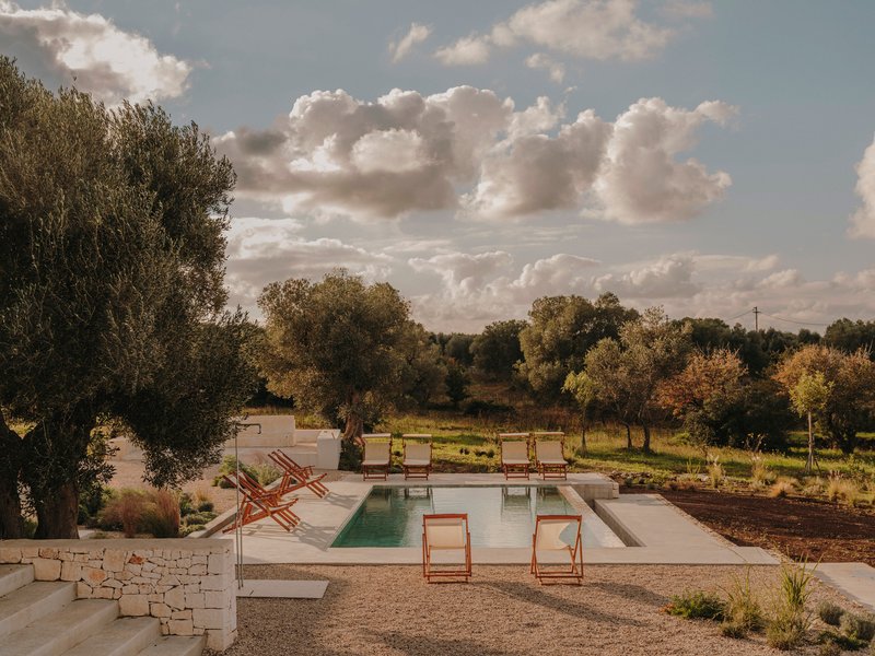 Pool terrace edged by dry stone walls with olive groves beyond under dramatic sky