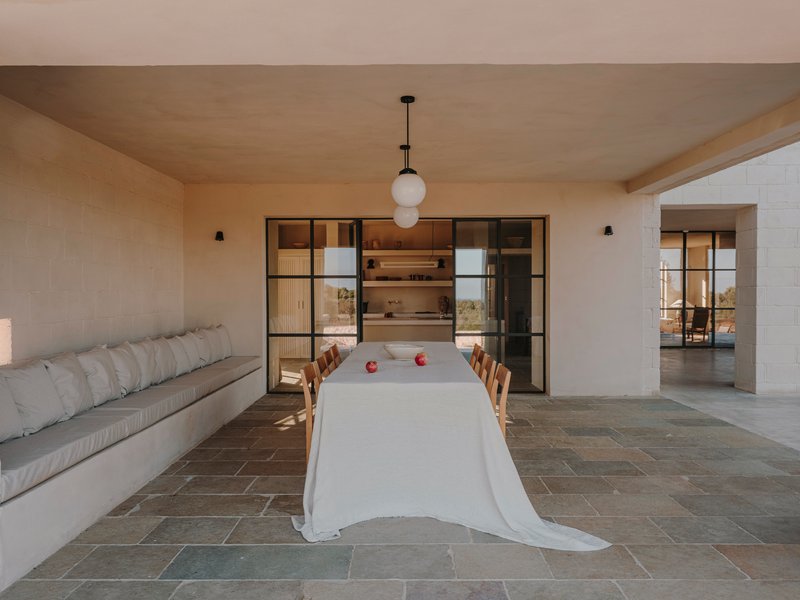 Open-plan dining room with steel-framed glass doors leading to the kitchen and stone tile floor