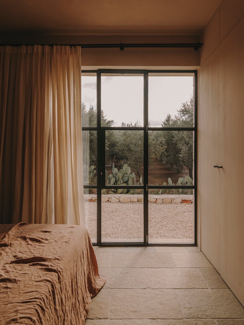 Steel-framed glass door opening to a gravel courtyard with potted cacti and olive trees