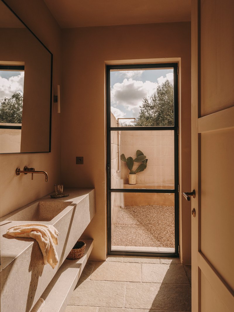 Bathroom with travertine vanity and black-framed door to an enclosed patio under billowing clouds