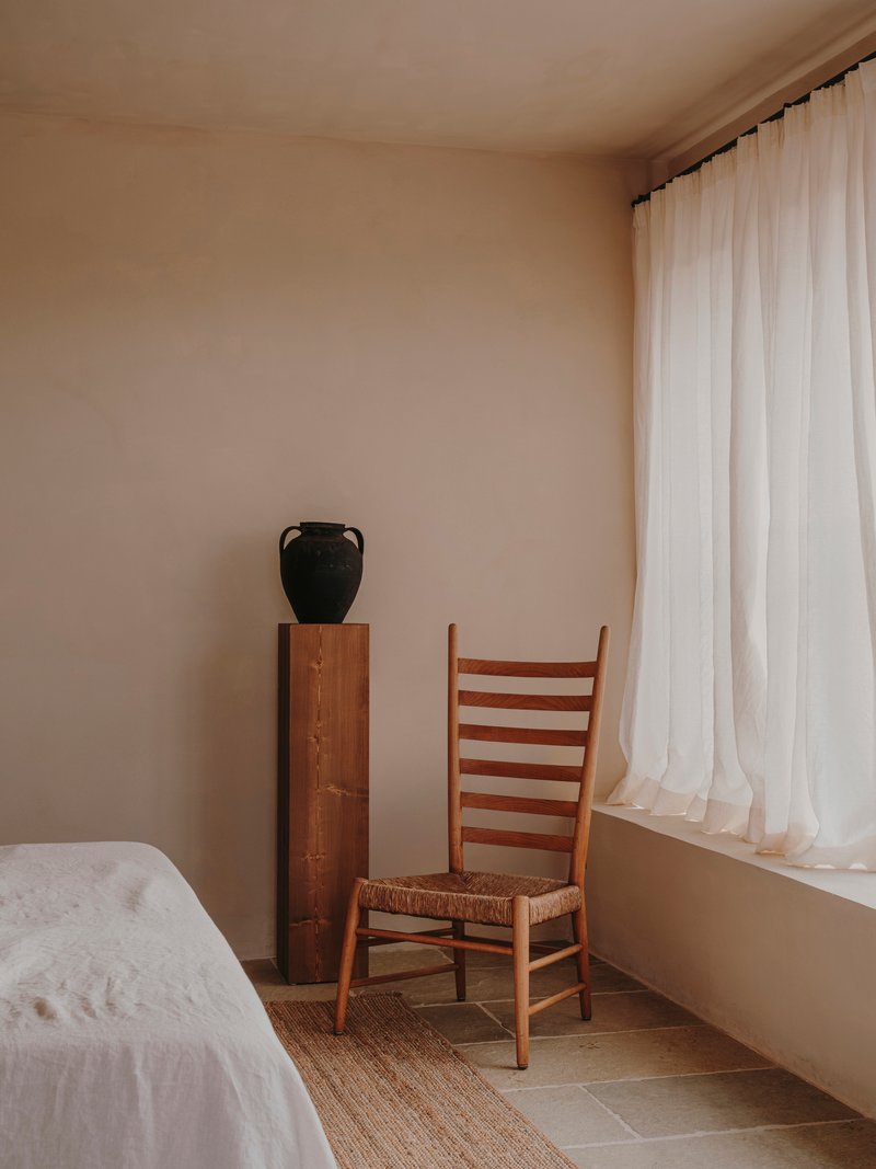 Bedroom corner detail showing a woven-seat chair and black vessel on an inlaid timber cabinet