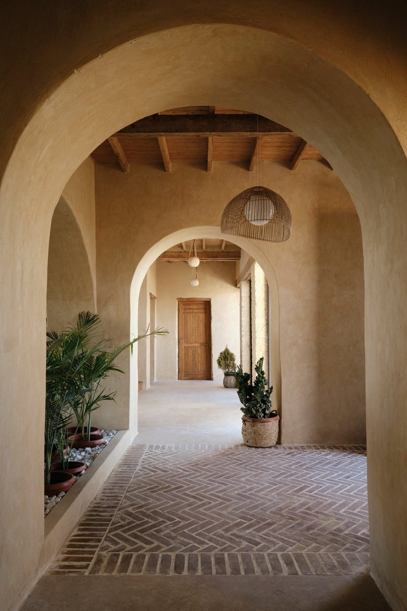 Sequence of plastered arches along a herringbone brick floor with potted plants