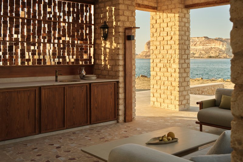 Open-air lounge with perforated brick screen wall and timber credenza overlooking calm water