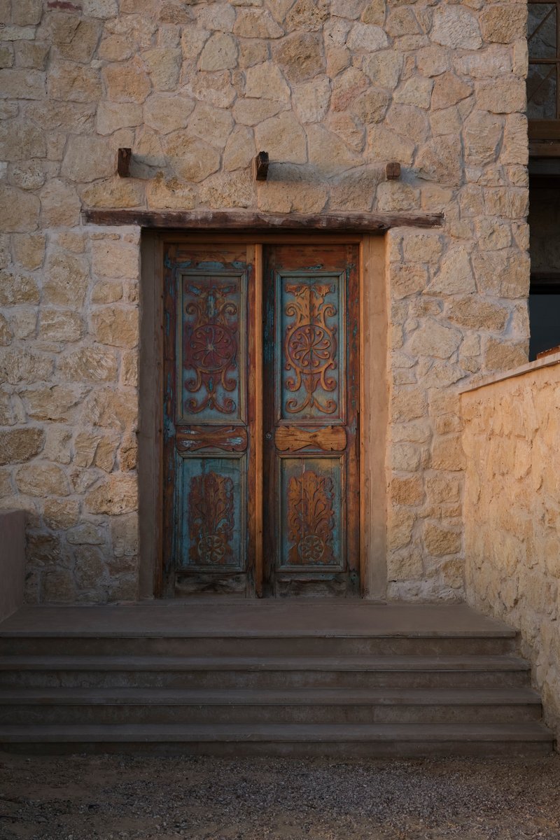 Weathered painted wooden double doors set into a coursed stone wall with timber lintel and iron brackets