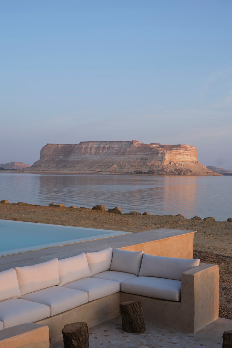 Sunken limestone seating area beside a pool with stratified rock formations reflected in still water at dusk