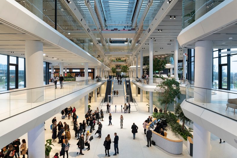 Central atrium hall with skylight above, multiple balcony levels and visitors congregating around planted planters below