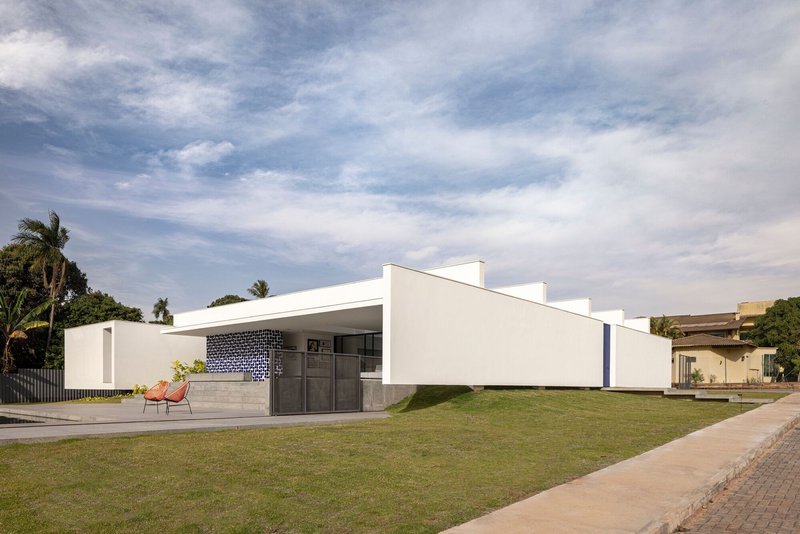 Street view of the white stucco facade with dark tiled portal and low concrete bench under palm trees