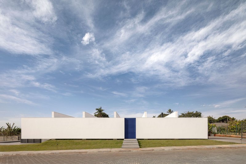 Long white facade with central blue door and stepped roofline against a cirrus cloud sky