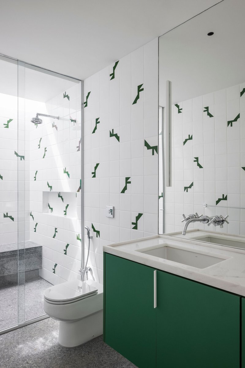 Bathroom with green vanity cabinetry, white tiled walls decorated with dark green geometric decals, and terrazzo flooring