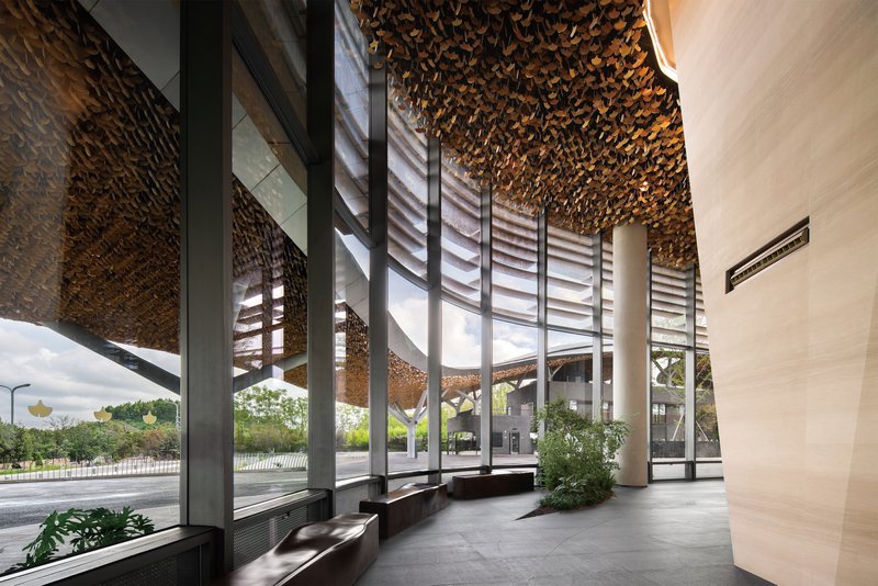Interior lobby with glass curtain walls, louvered screens, and golden ceiling beneath the canopy