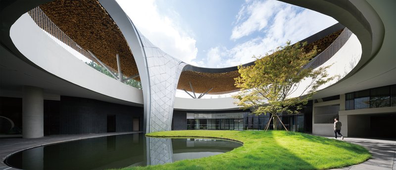 Interior courtyard with circular reflecting pool, lawn, and curved roof canopy overhead with planted soffit