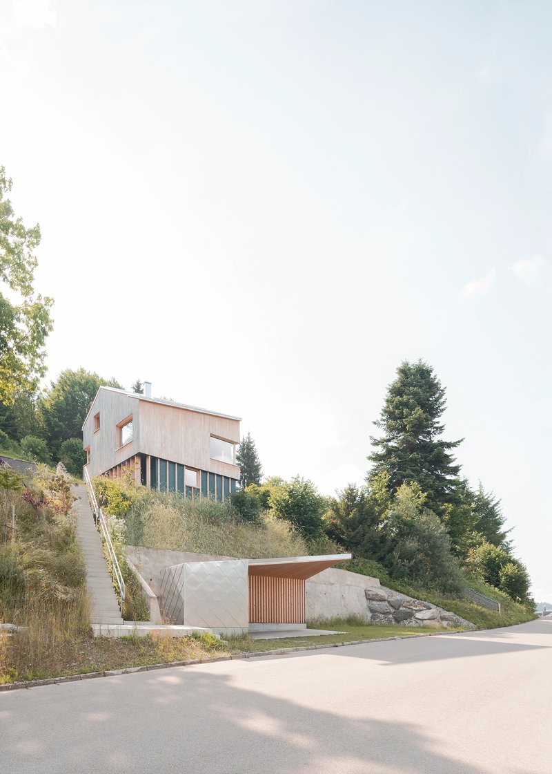 Hillside street view showing timber-clad upper volume on slats above concrete lower garage with slatted door