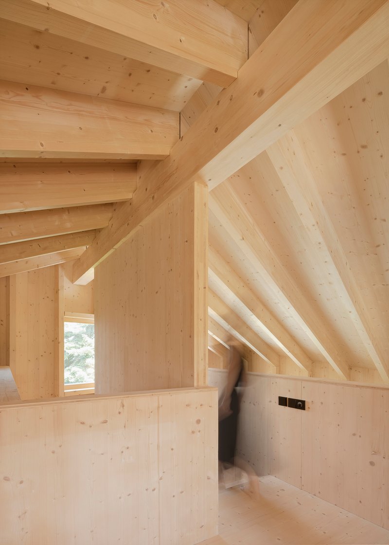 Interior room with exposed timber rafters and light wood walls with a blurred figure walking