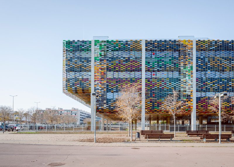 Long facade showing the pixelated screen with white structural columns and bare winter trees in foreground