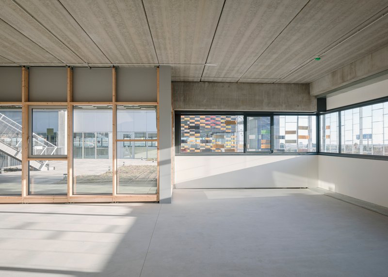 Interior space with board-formed concrete ceiling and floor-to-ceiling glazing overlooking the perforated ceramic facade