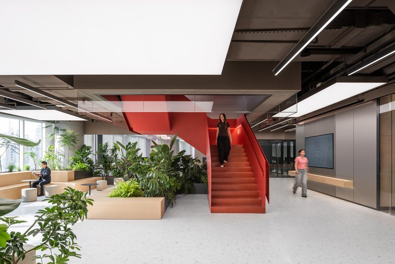 Red steel staircase rising through an office lobby with potted plants and exposed ceiling ducts