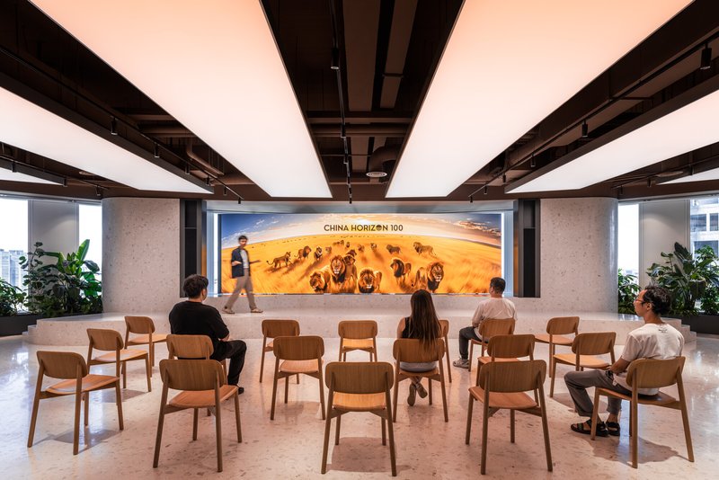 Wooden chairs arranged in rows facing a large illuminated photographic mural with people seated