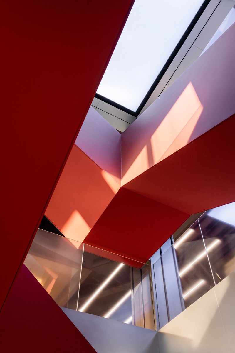 Upward view of a multi-story atrium with red-painted angular ceiling planes and a skylight above