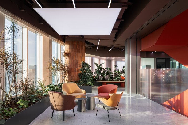 Lounge area with planted beds, upholstered chairs and a large skylight beneath an exposed black ceiling
