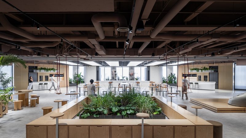 Communal workspace with raised timber planters, high tables and people gathering under an exposed ceiling structure