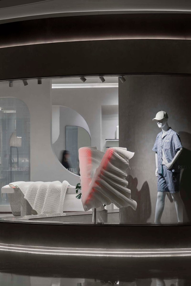 Display window with mannequin and textured sculptural element behind curved glass