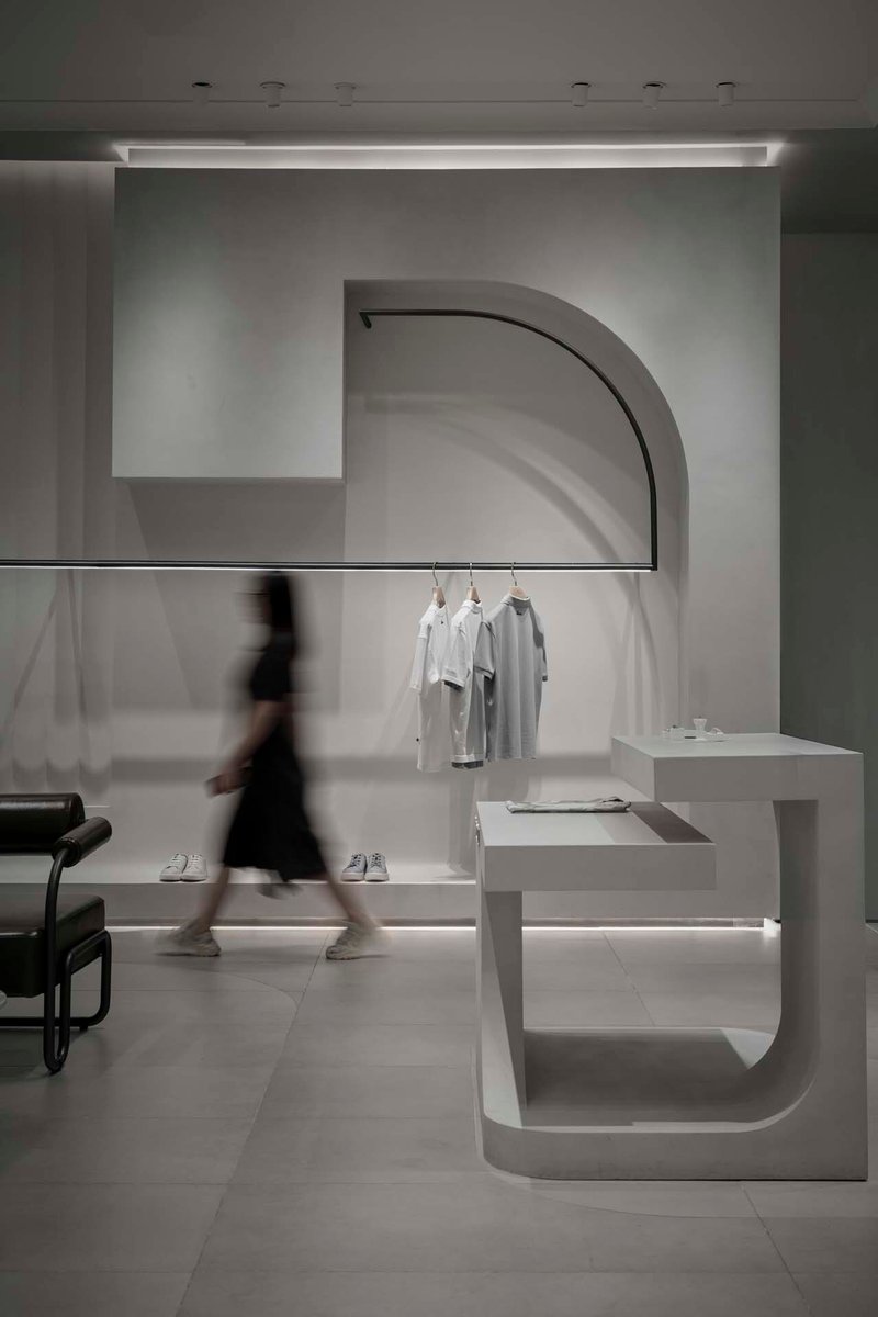 Arched display niche with clothing rack and blurred figure walking past white cantilevered platform