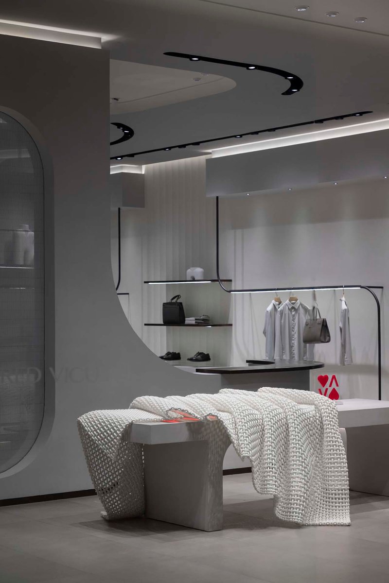 Display area with black curved ceiling track, glass shelving and upholstered seating in foreground