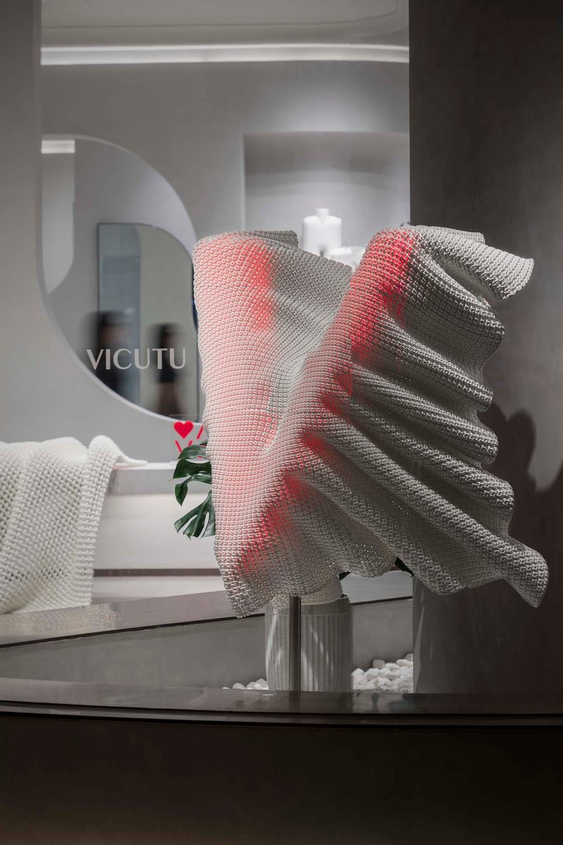 Close-up of red and grey mesh fabric sculpture on glass table beside circular mirror