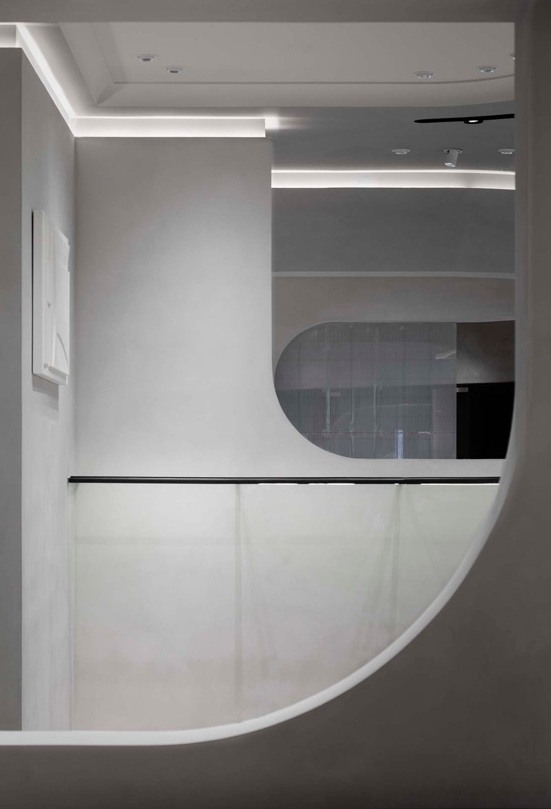 Curved white reception desk with black metal rail beneath horizontal strip lighting