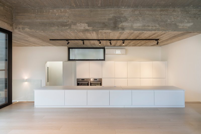 Kitchen with white island and wall cabinetry below board-formed concrete ceiling and black track lighting