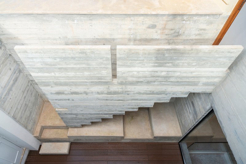 Overhead view of concrete stairs beneath a board-formed ceiling with natural light filtering through