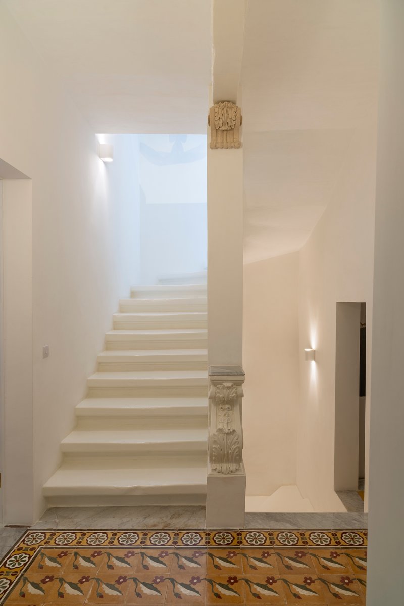 White plastered staircase with carved stone balustrade above decorative patterned floor tiles