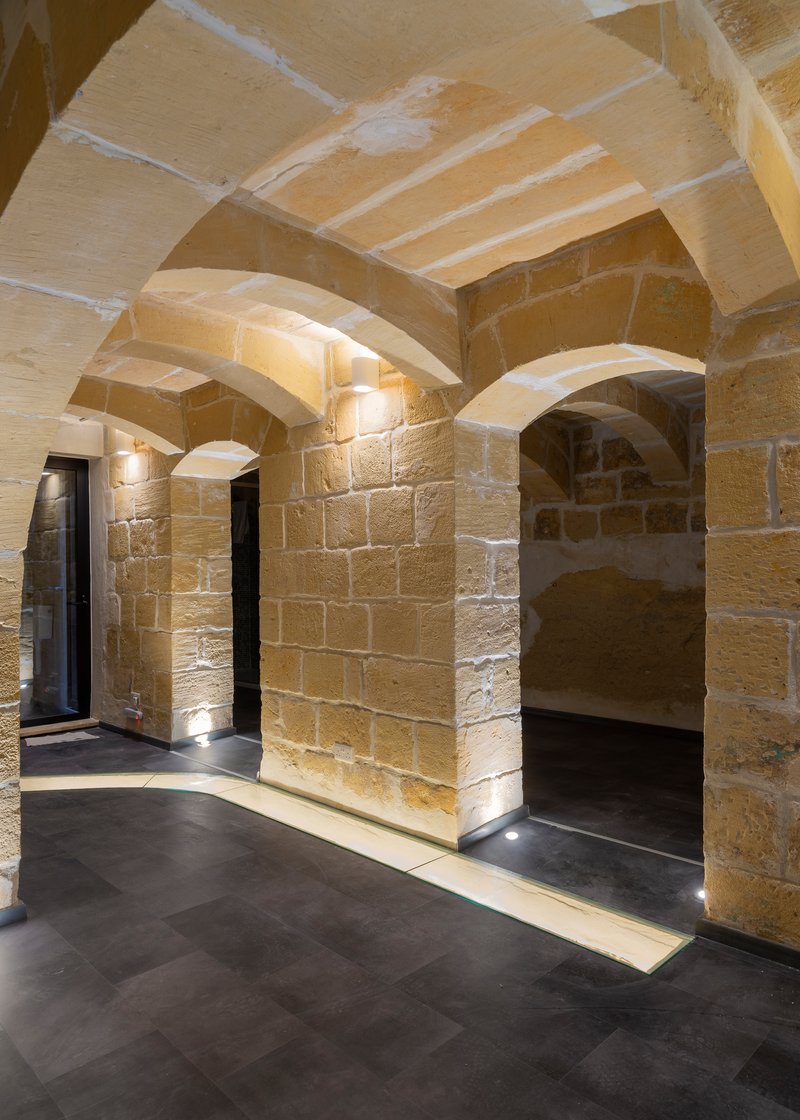 Vaulted sandstone corridor with exposed masonry walls and recessed floor lighting at night